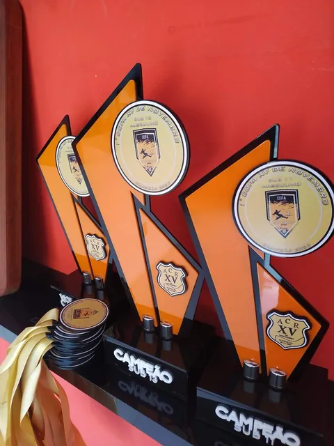 Troféus e medalhas em preto, laranja e dourado. Fotografia de trabalho da VLT Acrílicos.