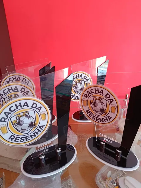 Troféus Rachada Resenha em branco e vermelho. Fotografia de trabalho da VLT Acrílicos.