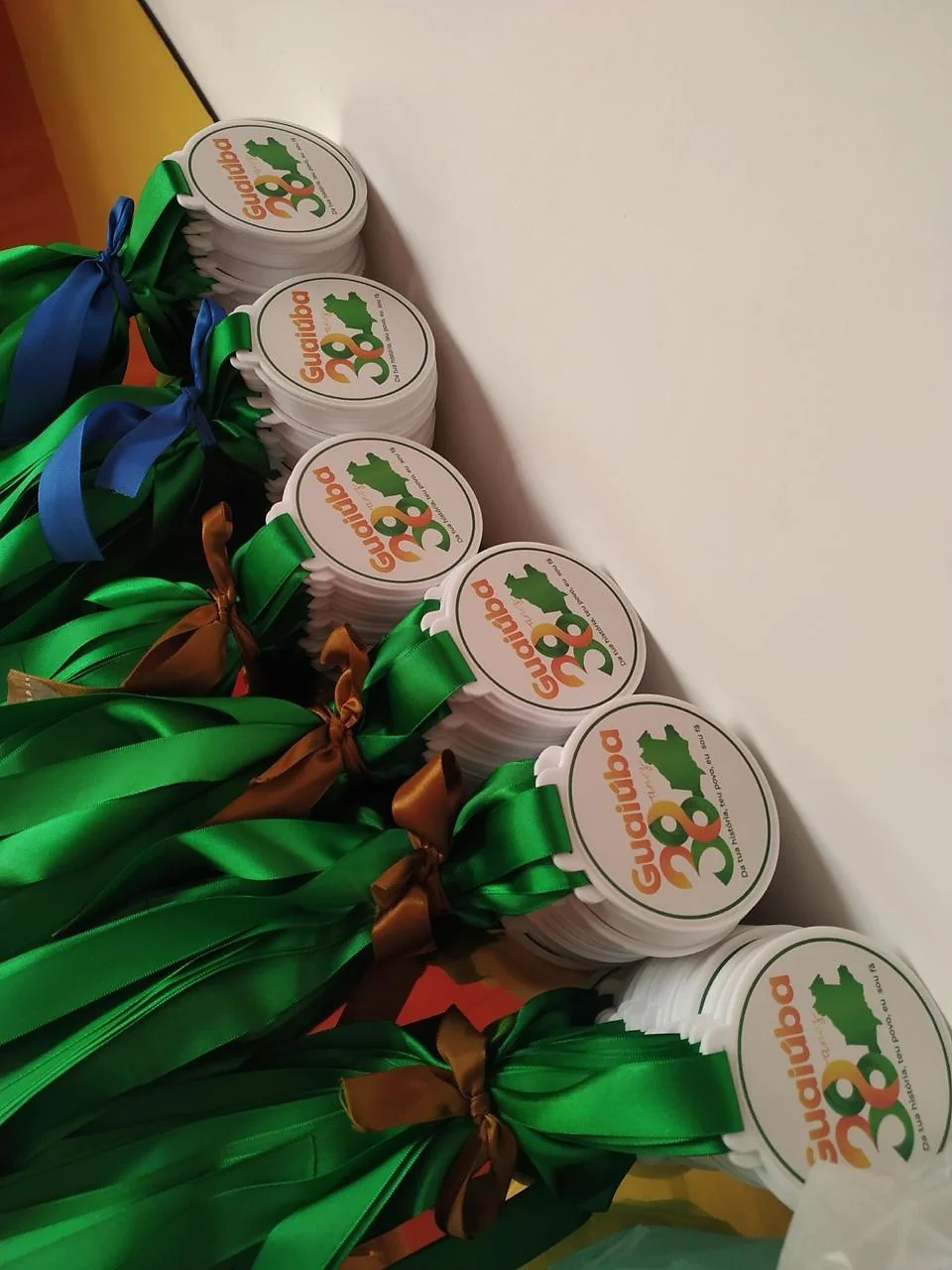 Medalhas com fitas verdes e azuis. Fotografia de trabalho da VLT Acrílicos.