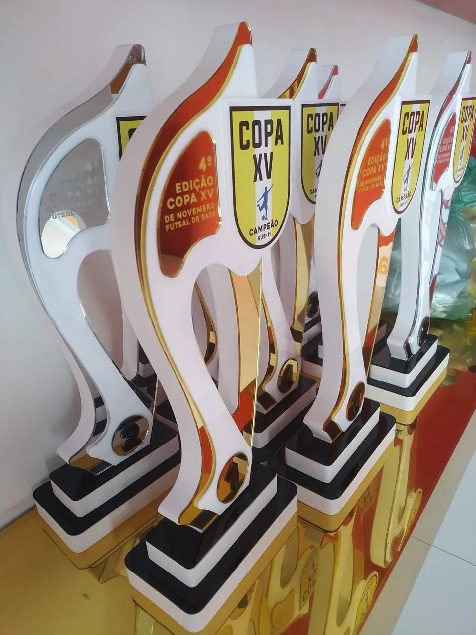 Troféus altos de futebol em branco, dourado e vermelho. Fotografia de trabalho da VLT Acrílicos.