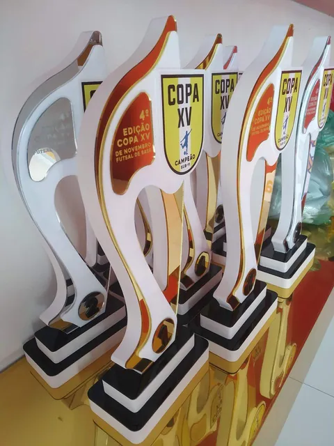 Troféus altos de futebol em branco, dourado e vermelho. Fotografia de trabalho da VLT Acrílicos.